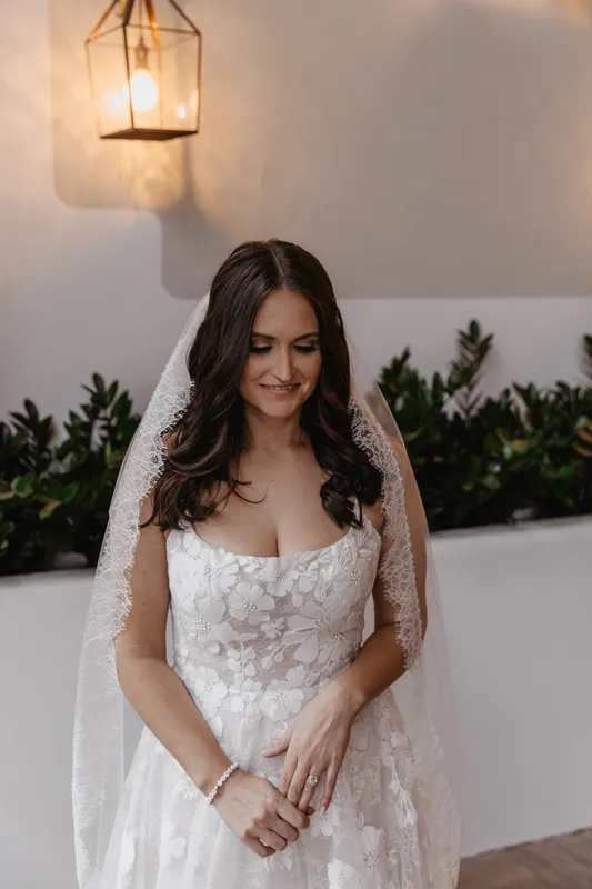 A beautiful bride with soft glam makeup wearing a white floral wedding dress and a delicate lace veil.