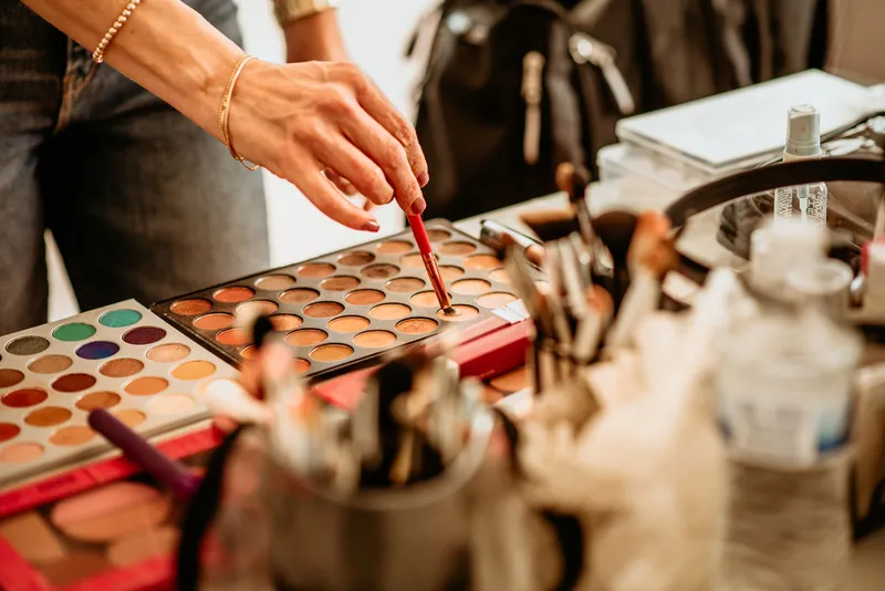 Makeup artist using a brush to pick a shade from a professional eyeshadow palette during a session.