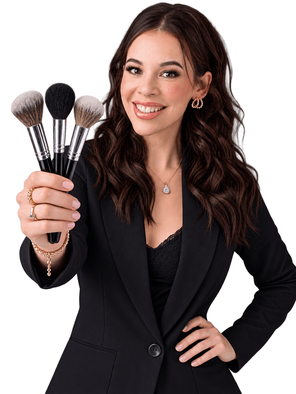 A smiling professional makeup artist holding three cosmetic brushes in front of a dark background.