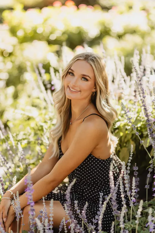 A blonde woman smiling in a black polka dot dress posing for professional senior portrait photography session.